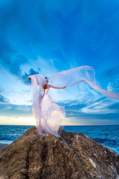 Jonge bruid door de zee bij zonsondergang — Stockfoto