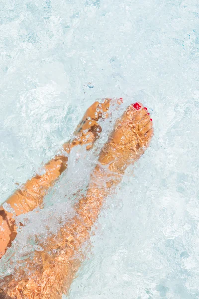 Pernas da menina na piscina fazendo salpicos — Fotografia de Stock