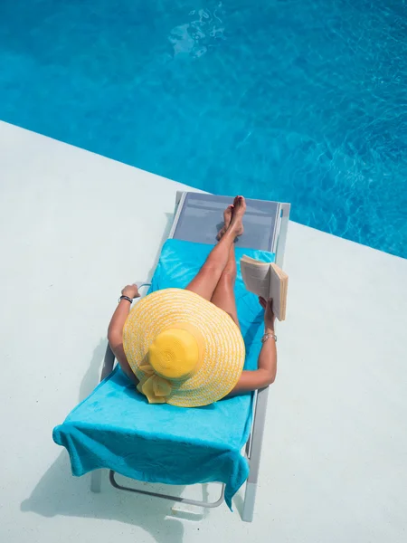 Mulher relaxante na piscina lendo um livro — Fotografia de Stock