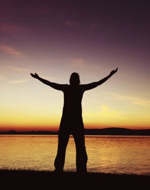 Gün batımında eğlenen ve eğlenen kolları açık bir kadın silueti.