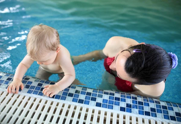 Woman helps baby at edge of swimming pool — Stock Photo, Image