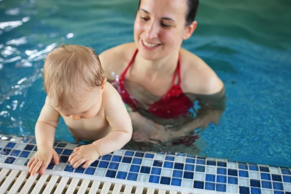 Woman helps baby at edge of swimming pool — Stock Photo, Image