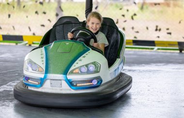 Gülen küçük çocuk lunaparkta çarpışan araba yolculuğunun tadını çıkarıyor. Bu canlı yaşam tarzı bir eğlence deneyimi sırasında neşeyi, heyecanı ve neşeli enerjiyi yakalar. Çocukluk mutluluğunu, eğlence aktivitelerini, aile eğlencesini mükemmel bir şekilde temsil ediyor.