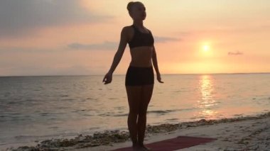Gün batımında plajda yoga yapan genç bir kadın.
