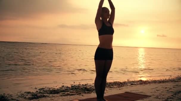 Gün batımında plajda yoga yapan genç bir kadın. — Stok video