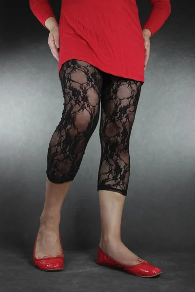 Жіночі ноги в чорних мереживних легінсах і червоній сукні над сірим ба — стокове фото
