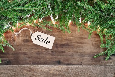 Çam iğneleri ve ahşap arka plan üzerinde satış etiketiyle ışıklar