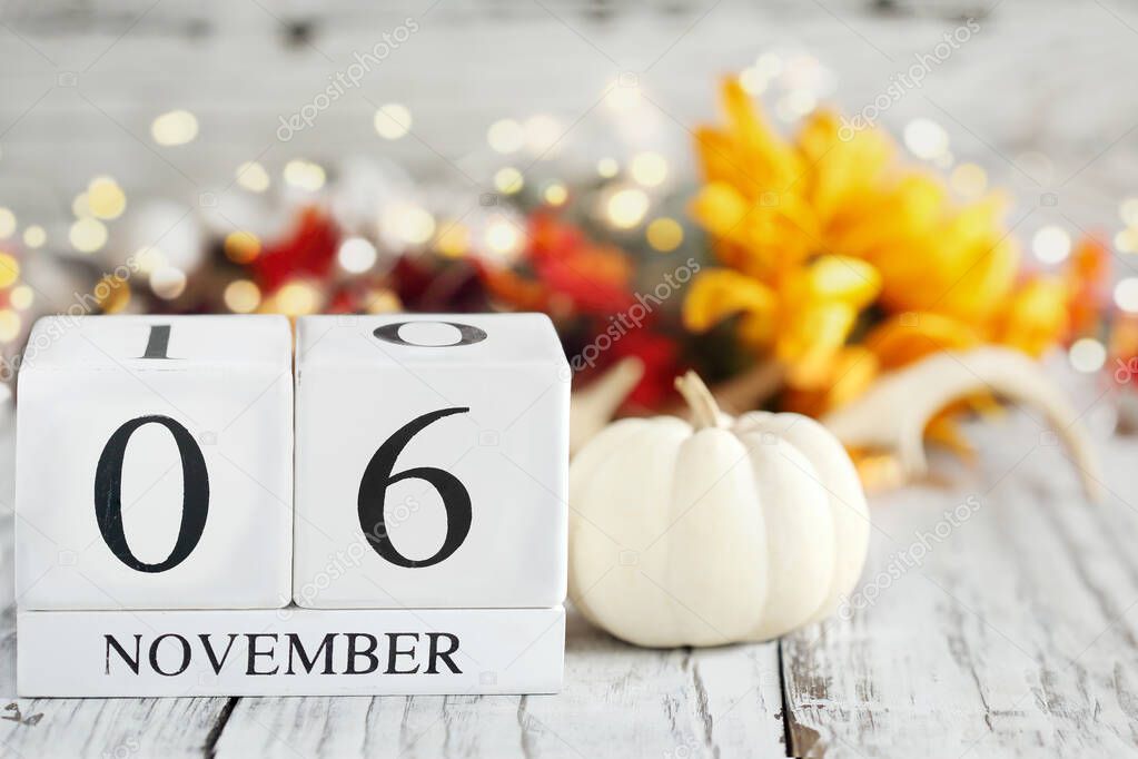 White wood calendar blocks with the date November 6th and autumn decorations over a wooden table. Selective focus with blurred background. 