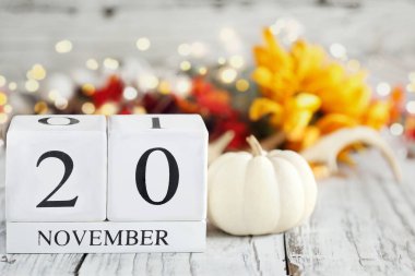 Tahta bir masanın üzerinde tarihi 20 Kasım ve sonbahar süslemeleri olan beyaz tahta takvim blokları. Bulanık arkaplan ile seçmeli odak. 