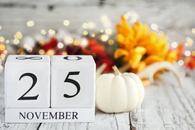 Tahta bir masanın üzerinde 25 Kasım ve sonbahar süslemeleri olan beyaz ahşap takvim blokları. Bulanık arkaplan ile seçmeli odak. 