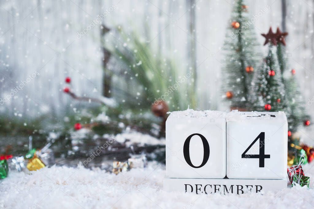 White wood calendar blocks with the date December 4th and Christmas decorations with snow. Selective focus with blurred background. 
