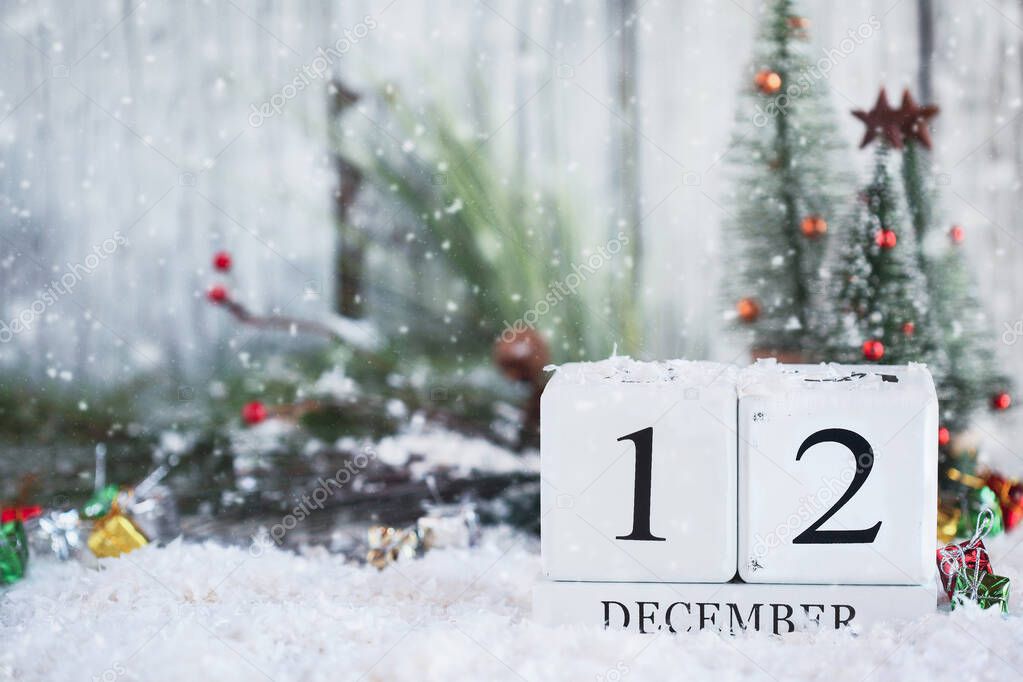 White wood calendar blocks with the date December 12th and Christmas decorations with snow. Selective focus with blurred background. 