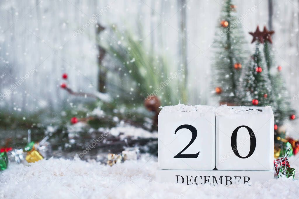 White wood calendar blocks with the date December 20th and Christmas decorations with snow. Selective focus with blurred background. 