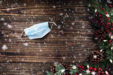 Noel ve Yeni Yıl kutlamaları tıbbi maske, Noel ağacı ışıkları, çam dalları, kırmızı kış meyveleri ve karla kutlanır. Kopyalama alanı olan üst görünüm.