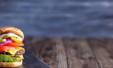 Büyük, yağlı, sulu bir çift çizburger% 100 sığır eti köftesi, erimiş peynir, soğan, turşu, marul, domates ve mayonez dilimleri ile yapılmış. Bulanık arkaplan ile sığ alan derinliği.