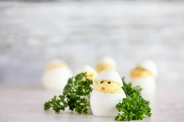 Deviled eggs for Easter decorated as cute little chicks hatching from eggs with carrot beak and seaweed eyes. Extreme shallow depth of field with blurred background and room for copy space.