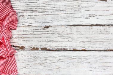 Boş bir beyaz ahşap piknik masasının üst görüntüsü ve sınırın kenarındaki buruşmuş kırmızı ve beyaz gingham masa örtüsü. Metin için boş alan. 