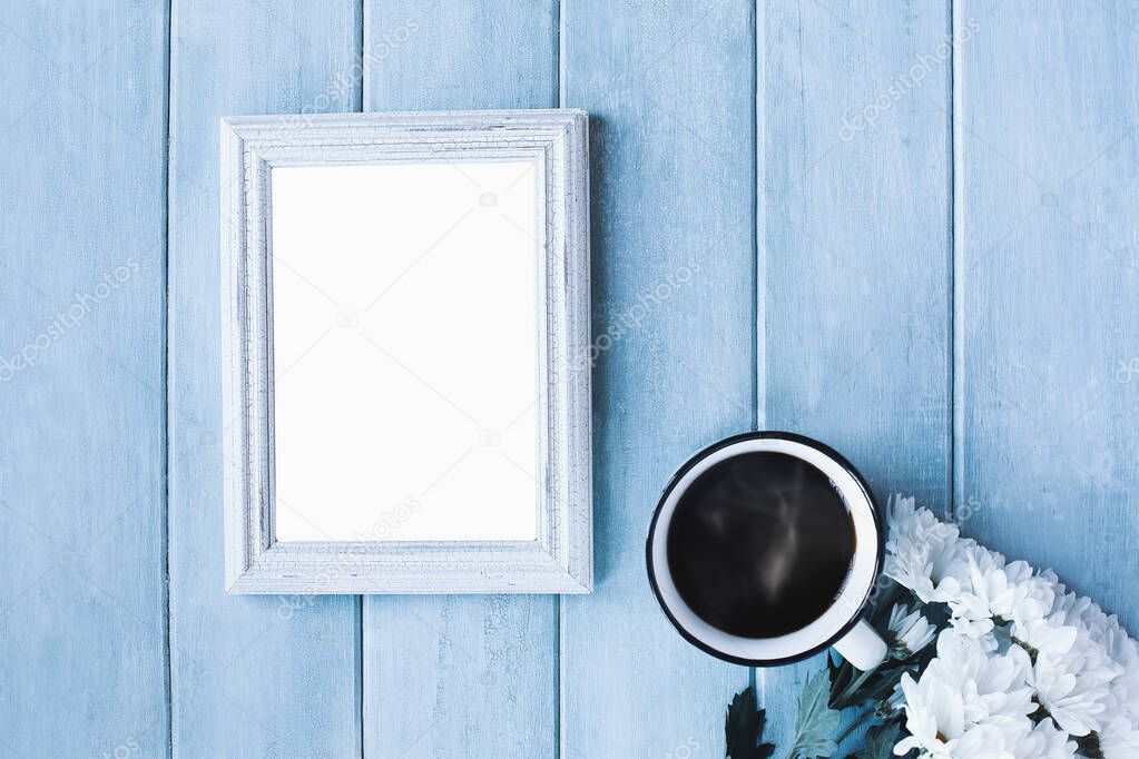 Blank vertical empty picture frame over blue rustic background with steaming coffee and white daisy flowers.