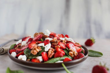 Bir tabak ev yapımı taze ıspanak yaprağı dilimlenmiş çilek, ceviz, peynir ve hafif sirke soslu salata. Son derece sığ alan derinliğine sahip seçici odak.