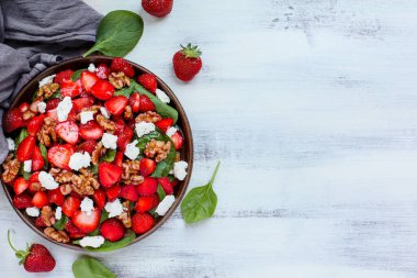 Bir tabak ev yapımı taze ıspanak yaprağı, dilimlenmiş çilek, ceviz, feta peyniri ve beyaz ahşap masa üzerinde servis edilen hafif vinaigrette sosu.. 