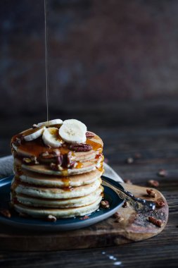 Kreplerin üzerine akçaağaç şurubu dökülüyor. Taze muz ve fındık ile servis ediliyor. Bulanık arkaplan ve arkaplan ile seçmeli odak.