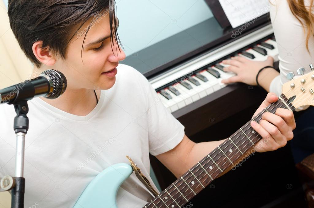 Teenage boy playing electric guitar and singing girl piano