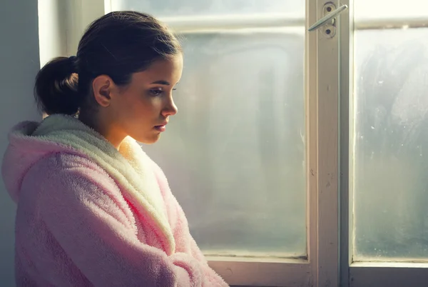 Sjuk ledsen flicka i pyjamas titta igenom sjukhus fönster — Stockfoto