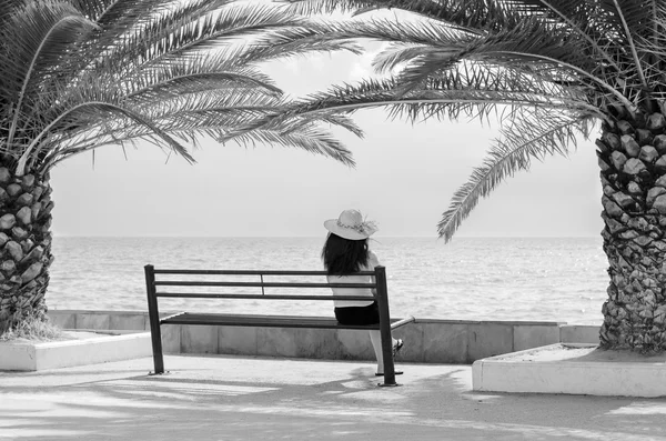 Юная леди сидит на скамейке и смотрит на летнее море — стоковое фото