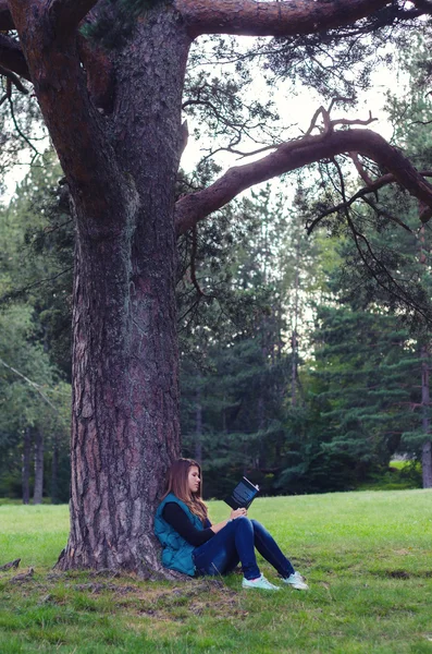 Adolescente sentada debajo del árbol y leyendo el libro —  Fotos de Stock
