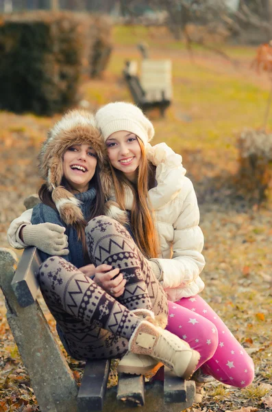 Zwei schöne Mädchen sitzen auf der Bank im Freien im sonnigen Herbst — Stockfoto