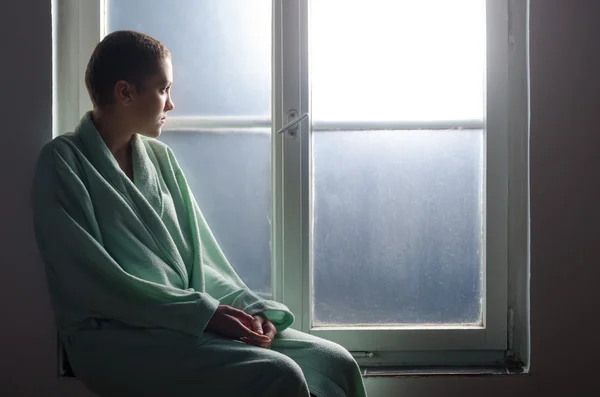 Молодий пацієнт з раком сидить перед вікном лікарні Ліцензійні Стокові Зображення