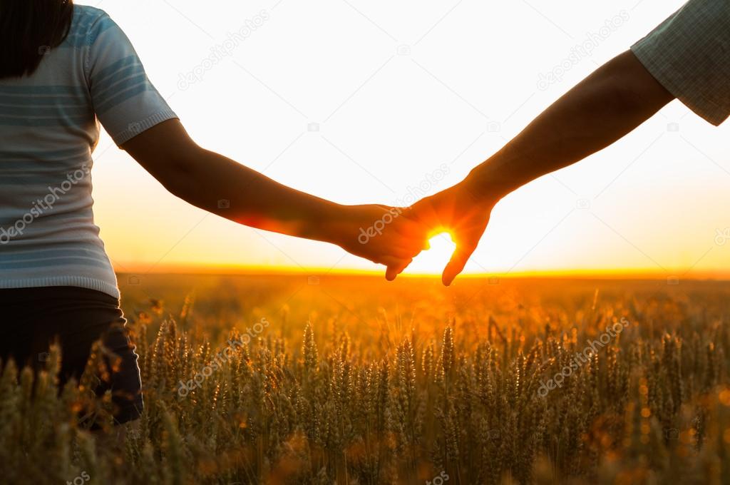 Young couple holding hands in the wheat field on sunny summer da