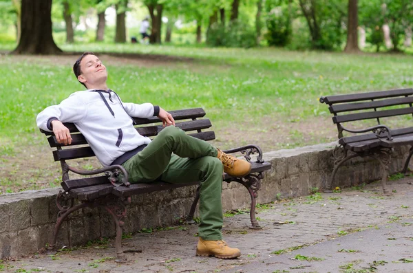 Jovem sentado no banco no parque e desfrutando de beautifu — Fotografia de Stock