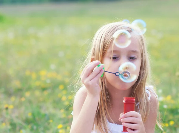 Маленька дівчинка дме мильні бульбашки на весняному лузі Стокове Зображення