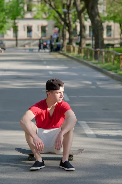 Handsome teenage boy sitting on skateboard in the middle of the