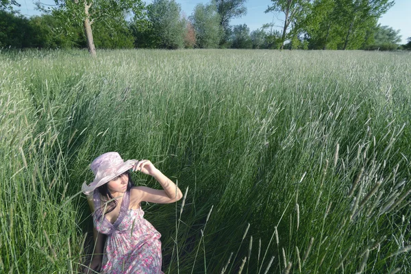 Schöne Mädchen sitzt im hohen Gras auf der Wiese auf sonnigem spri — Stockfoto