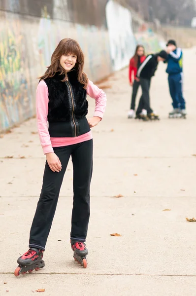 Hübsches lächelndes Mädchen auf Rollschuhen posiert im Herbst mit Freunden im Freien — Stockfoto