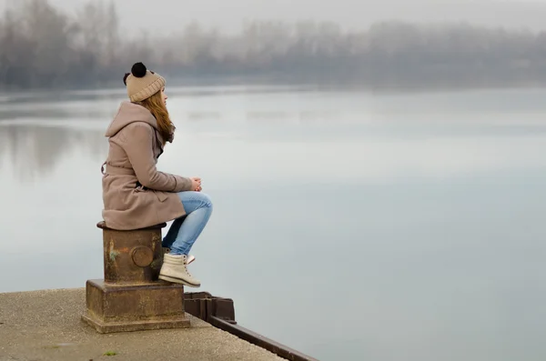 Lonely sad teenage girl sitting on the dock on cold winter day — Stock Photo, Image