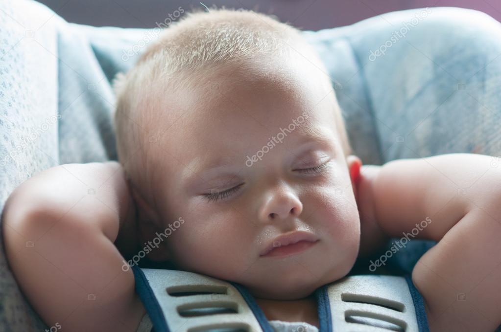 Infant boy sleeps peacefully secured with seat belts while in the car