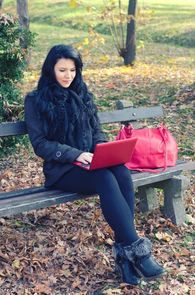 Beautiful happy girl using notebook while sitting in autumn park — Stock Photo, Image