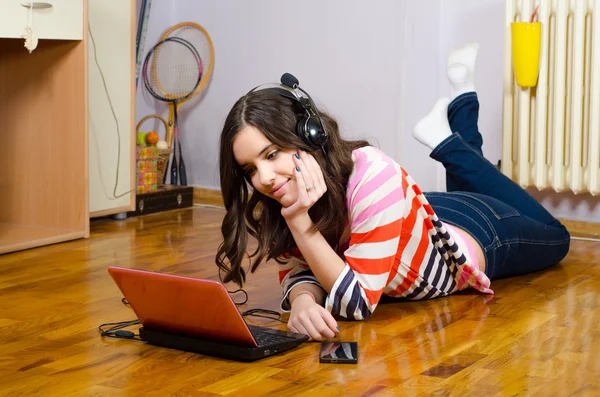 Beautiful teenage girl listening to music while lying on floor — Stock Photo, Image