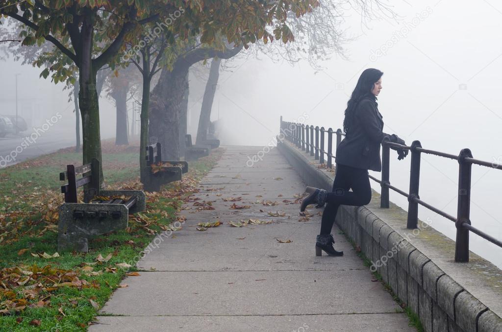 Beautiful girl standing on pedestrian walkway watching autumn mist