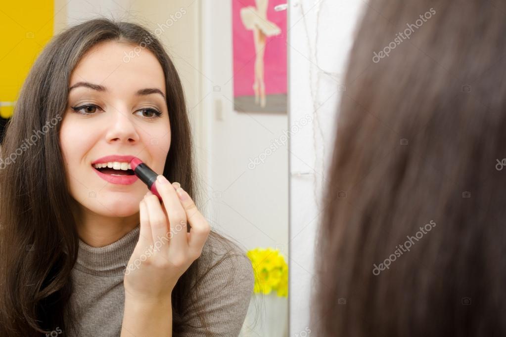 Beautiful girl putting lipstick in front of the mirror Stock Photo by