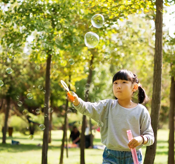 Girl blowing soap bubbles at park — Stock Photo, Image