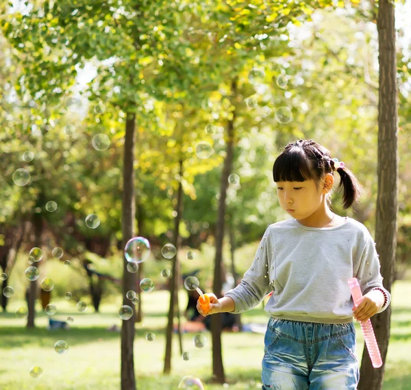 Chica soplando burbujas de jabón en el parque —  Fotos de Stock