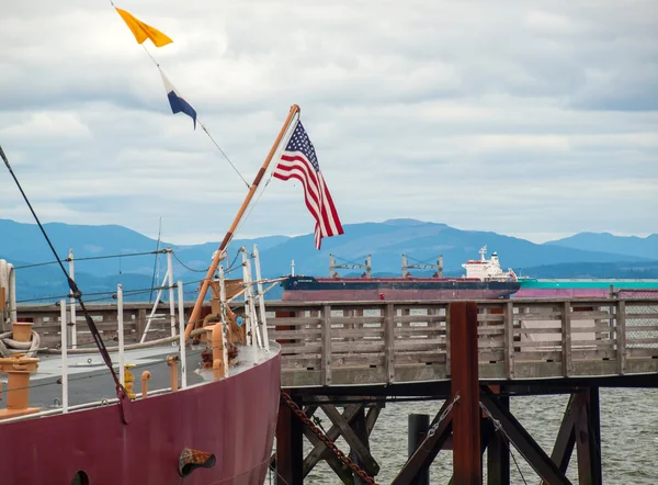 Bandera americana colgando en muelles con buque de carga en la bahía —  Fotos de Stock