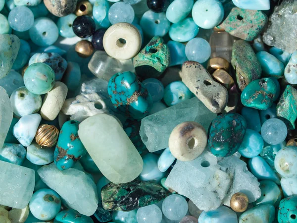 Natural polish textured sea glass and stones on the seashore. Azure clear sea water with waves. Green, blue shiny glass with multi-colored sea pebbles close-up.