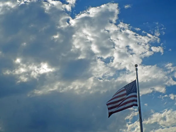 A bandeira americana pendurada antes de nuvens e raios de sol — Fotografia de Stock