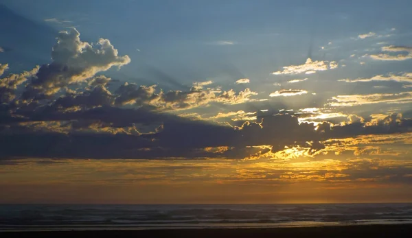 Облачный закат над океаном с солнечными лучами в небе — стоковое фото