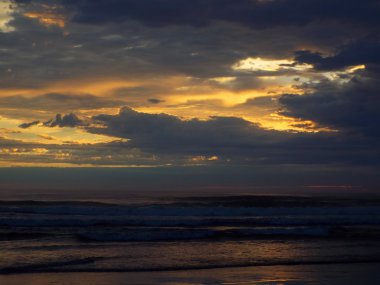 Okyanus dalgaları ön planda ile bulutlu gün batımı